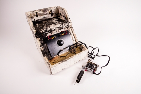 Small white box covered in ink stains with a tattoo machine attached by cord.