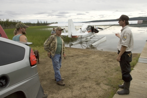 Two men in green and camouflage clothes talk to a Service employee in uniform by an airboat