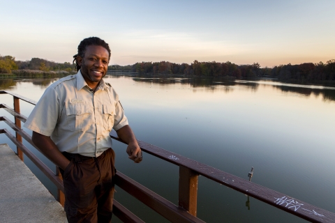 Uniformed employee leans against the railing on a dock in front of a body of water at dusk