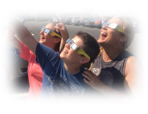 Three people wearing solar eclipse viewing glasses look up towards the sun.