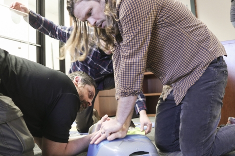 Two people practice CPR on a practice dummy while a third watches