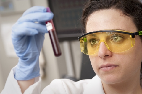 A woman scientist holds up and looks at a vial of blood.