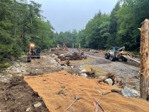 Heavy machinery constructing a new riverine floodplain with soil, gravel, logs, and boulders on the Narraguagus river in Beddington, Maine