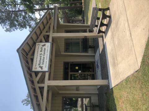 Image of front of building with double glass doors and sign above doors that says "Richard S Bolt Visitor Center" with a bench and sidewalk in foreground