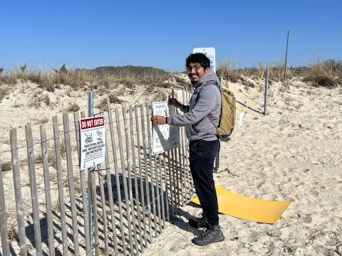 A smiling man posts a sign on a snow fence.
