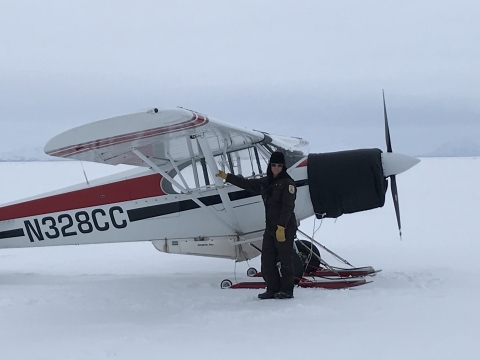 Pilot Kara Hilwig on a flat snow covered landscape with a Top Cub bush plane outfitted with skis. 