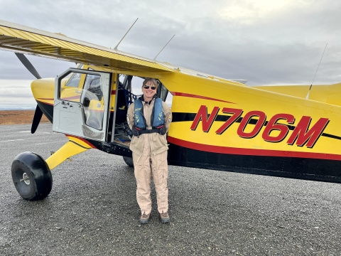 Kara Hilwig standing next to a single engine bush plane on a dirt airstrip. 