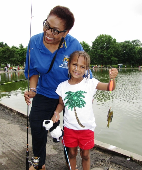A woman and little girl holding fishing poles and a fish.