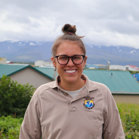Maria Fosado in NWRS uniform poses for a picture with a cloud covered mountain in the background and out of focus buildings. 