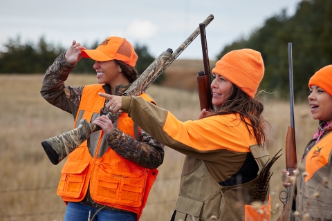 three women wearing orange stand together with long guns