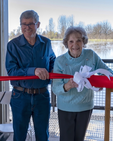Two people stand together, preparing to cut a large ribbon.