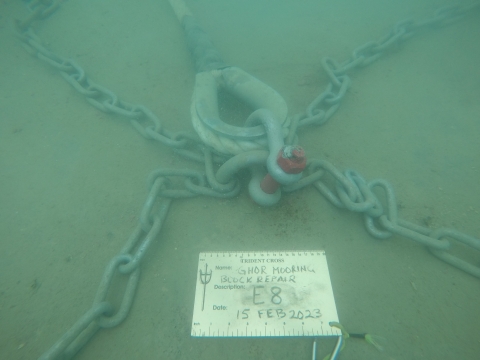 A picture of an underwater mooring in Guam's Harbor of Refuge. There are chains holding down a block of cement, and a sign on the cement labeling the block as in need of repair. 