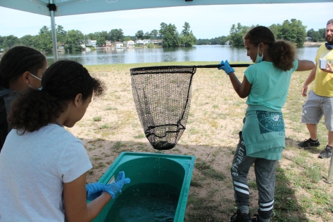 a student holds a net and wears gloves near other students looking into a tank