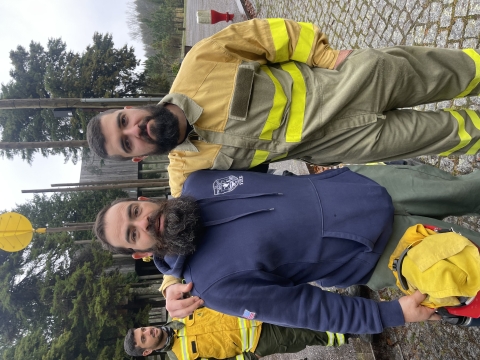 Two firefighters stand with their arms around each other facing the camera for a photo