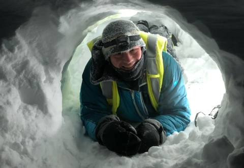 Image of individual at the mouth of a small snow den.