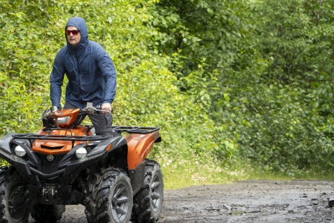 An ATV with a single rider on a muddy trail in a wooded area in the rain.