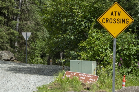 A trail head with an ATV Crossing sign in a wooded area. 
