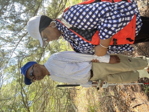 A man and a woman stand respectfully near trees. Their ancestors were part of the Gullah-Geechee community that once lived at what is now Harris Neck Refuge.