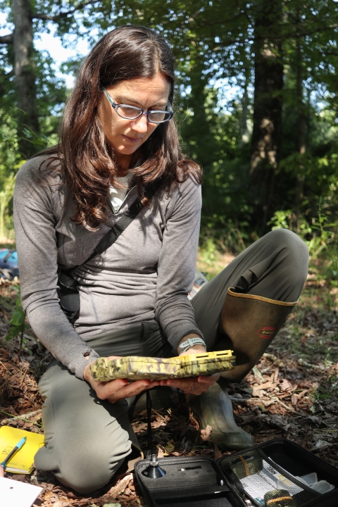 Woman kneeling on the ground looking at an electronic device in her hand