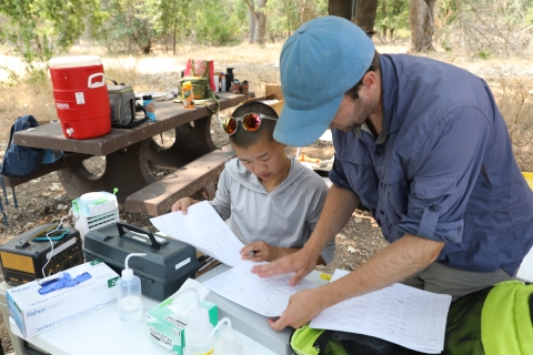 Two people look at paperwork surrounded by equipment in the outdoors