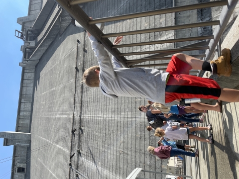Several kids below a dam looking over railing.