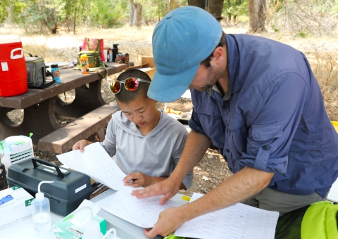 Two people look at data sheets in an outdoor camp setting
