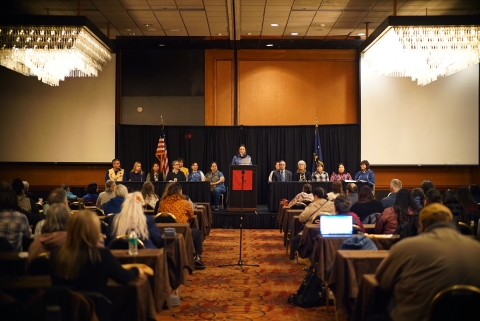 an audience looks up an isle to a speaker with flags on either side