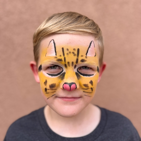 a blond child with their face painted to look like an ocelot