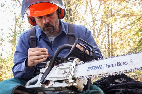 Person holding a small screwdriver to a chainsaw