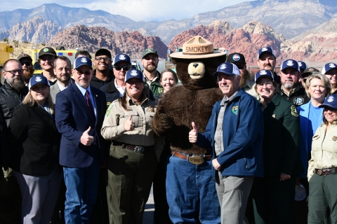 A group of uniformed officials pose with a Smokey mascot
