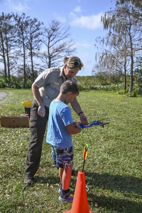 Ranger stands with a child preparing to load his bow and arrow