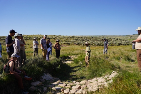 Clint Wirick, a Partners for Fish and Wildlife biologist stands in a gully, behind a one rock dam. On both sides of the gully are members of the Utah Watershed Restoration Initiative. 