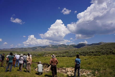 Conservation partners stand above an erosion control structure and overlook a field of sage backdropped by mountains.