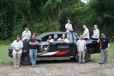 Several people pose in and around a black pickup truck parked near vegetation