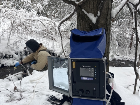 Image of person in winter attire holding a tube in a stream.