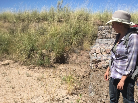 A researcher stands by a structure of rocks on a field