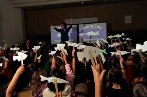 Children holding up paper fish on popsicle sticks with an instructor in a room