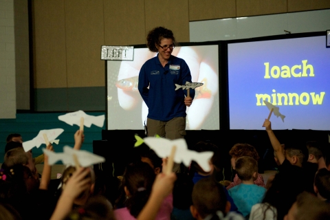 An instructor standing in front of a screen that says "Loach Minnow" in front of a group of kids