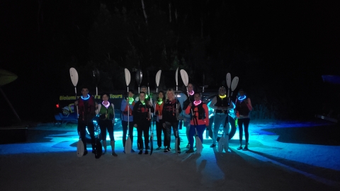 In the dark of night, participants in a bioluminescent kayak tour at Merritt Island Refuge stand next to their paddles.