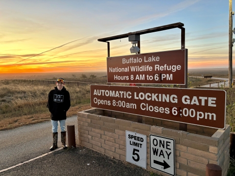 Youth boy standing next to the entrance gate of the Buffalo Lake National Wildlife Refuge with a sunset in the background 