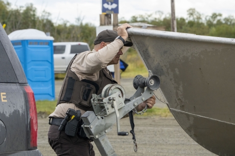 Federal Wildlife Officer connects a winch chain to the bow of a boat 