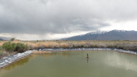 A small square research pond is in the foreground with large mountains in the background.