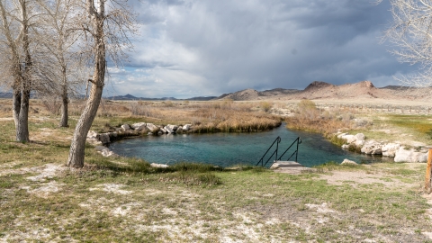 A small body of water with trees around it and a sagebrush landscape in the background.