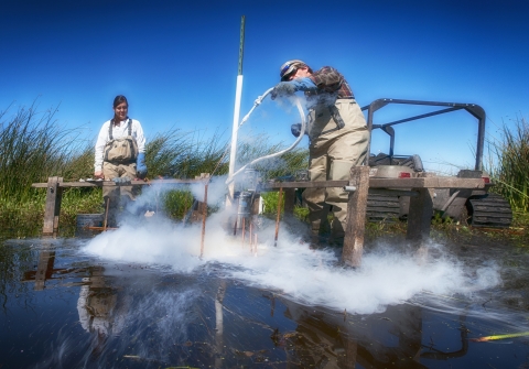 Two Bureau of Land Management employees sample soil by a wetland.
