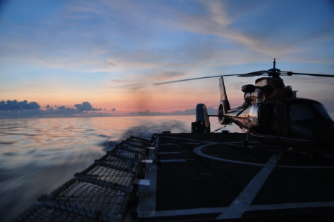 a sunset view of a flight deck area of a coast guard vessel with a helicopter on the flight deck. 