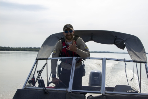 A uniformed officer offers a smile and shaka as he speeds along at the helm of a boat on a large river