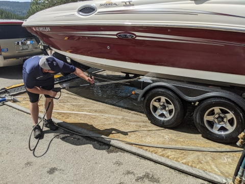 A man uses a pressure washer on a boats bottom.