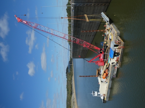 A crane on a barge lowers a portion of a bioacoustic fish fence into water.