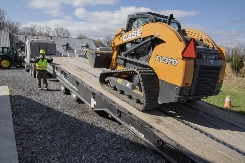 worker directs machinery onto truck trailer