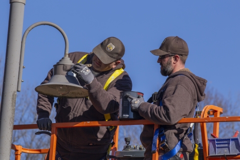 Wage grade employees modifying light fixture to focus light on ground.